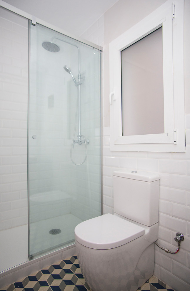 This is an example of a medium sized contemporary ensuite bathroom in Barcelona with light wood cabinets, an alcove shower, a one-piece toilet, white tiles, white walls, a vessel sink, multi-coloured floors and a sliding door.