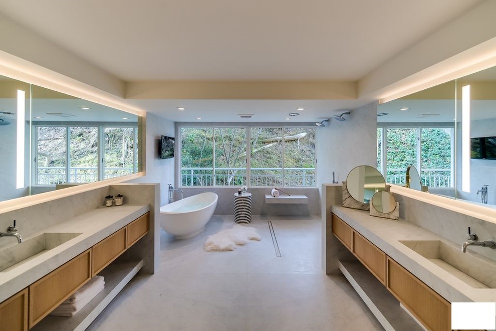 Modern inredning av ett mycket stort vit vitt en-suite badrum, med luckor med profilerade fronter, bruna skåp, ett fristående badkar, en kantlös dusch, en vägghängd toalettstol, grå kakel, cementkakel, vita väggar, betonggolv, ett avlångt handfat, bänkskiva i kvarts, grått golv och med dusch som är öppen