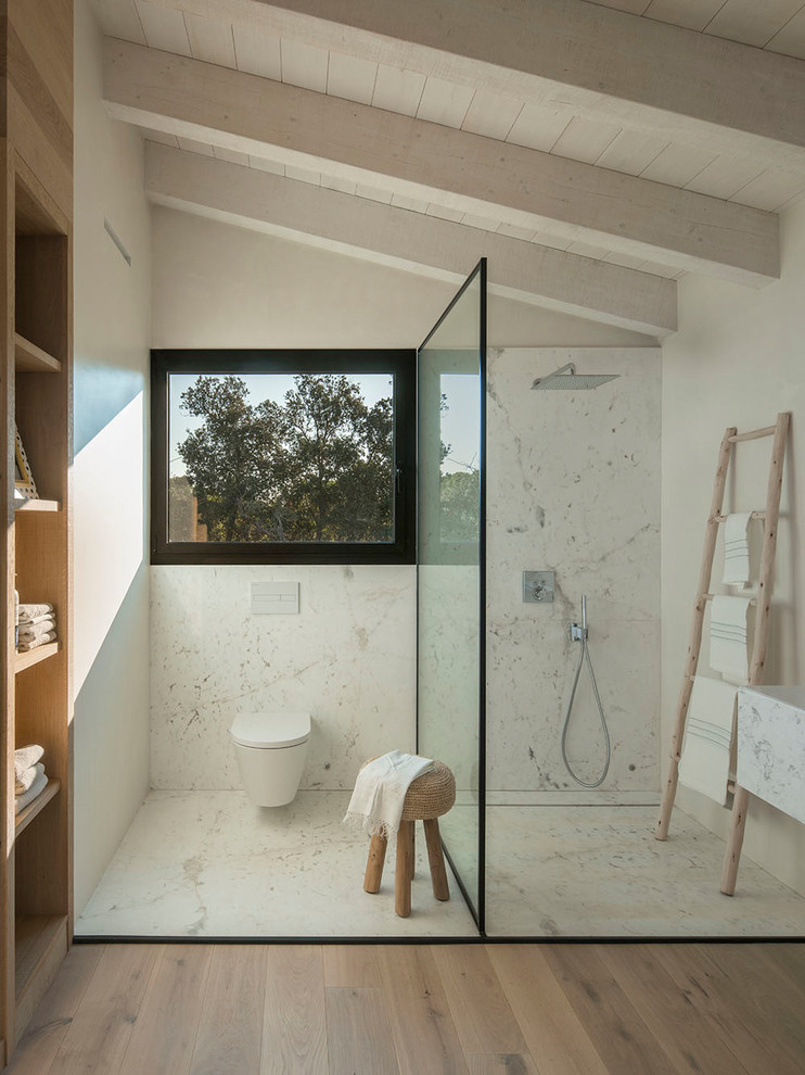 Modernes Badezimmer mit freistehender Badewanne, Duschbadewanne, Toilette mit Aufsatzspülkasten, weißen Fliesen, weißer Wandfarbe, braunem Holzboden und offener Dusche in Barcelona