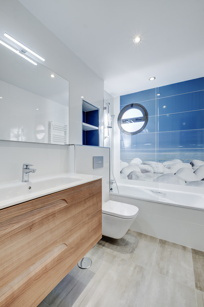 Inspiration for a contemporary master blue tile drop-in bathtub remodel in Madrid with medium tone wood cabinets, a wall-mount toilet, a trough sink, white countertops and flat-panel cabinets