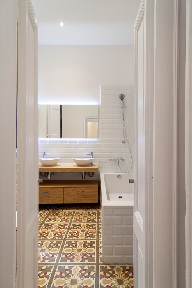 На фото: главная ванная комната среднего размера в скандинавском стиле с плоскими фасадами, фасадами цвета дерева среднего тона, ванной в нише, душем над ванной, белыми стенами, полом из керамической плитки и настольной раковиной с