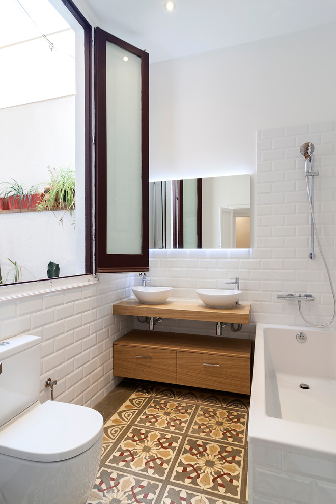 Idéer för ett mellanstort minimalistiskt brun en-suite badrum, med släta luckor, skåp i mellenmörkt trä, ett badkar i en alkov, en dusch/badkar-kombination, en toalettstol med separat cisternkåpa, vit kakel, tunnelbanekakel, vita väggar, klinkergolv i keramik, ett fristående handfat, träbänkskiva och med dusch som är öppen