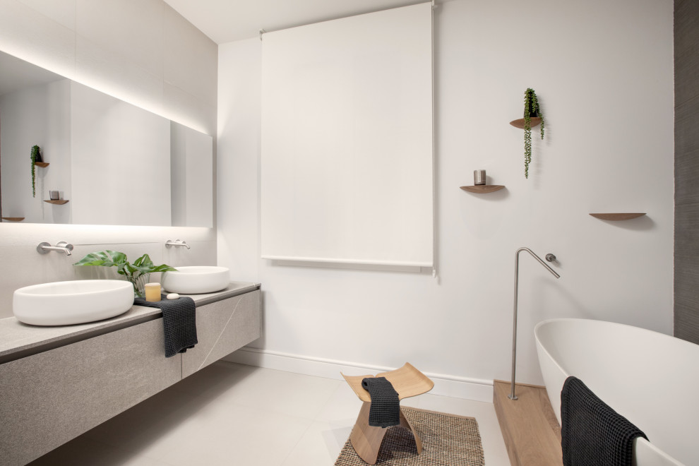 Inredning av ett modernt grå grått badrum, med släta luckor, grå skåp, vita väggar, ett fristående handfat och grått golv