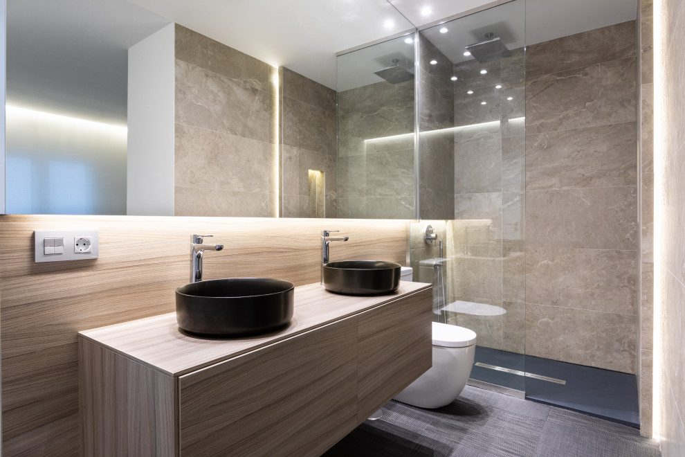 Foto på ett mellanstort funkis beige badrum med dusch, med släta luckor, beige skåp, en öppen dusch, en toalettstol med hel cisternkåpa, beige kakel, porslinskakel, vita väggar, ett fristående handfat, träbänkskiva och grått golv