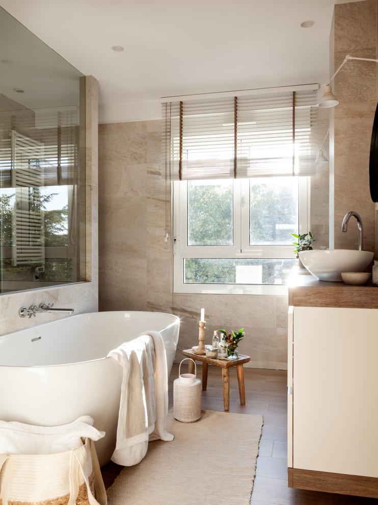 Пример оригинального дизайна: главная ванная комната среднего размера в стиле неоклассика (современная классика) с отдельно стоящей ванной, бежевой плиткой, настольной раковиной и бежевым полом