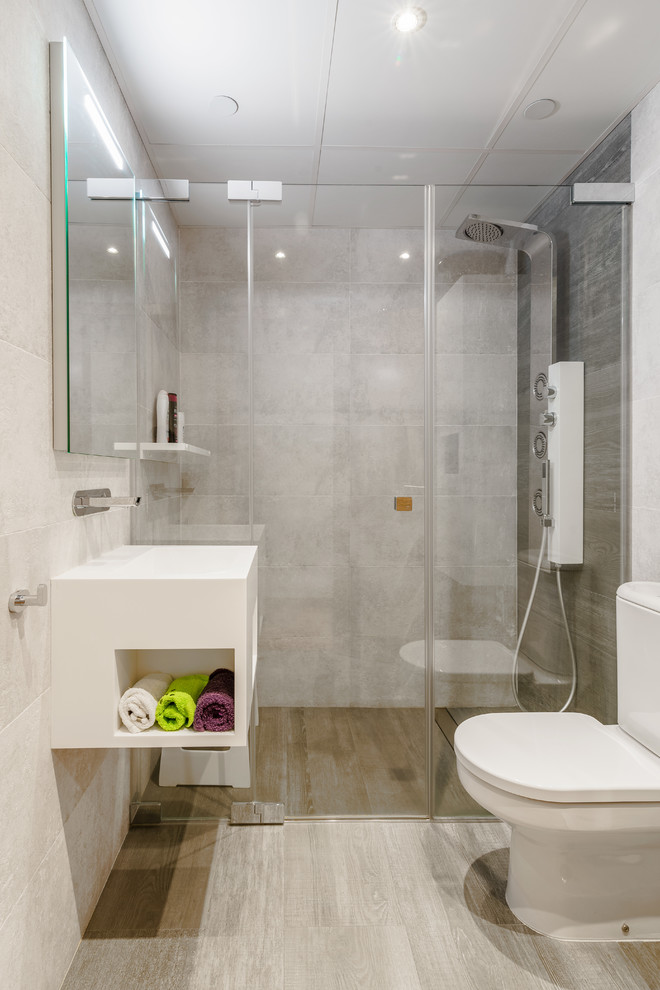 Cette image montre une salle de bain design avec des portes de placard blanches, WC séparés, un carrelage gris, un mur beige, un lavabo suspendu, un sol beige et une cabine de douche à porte battante.
