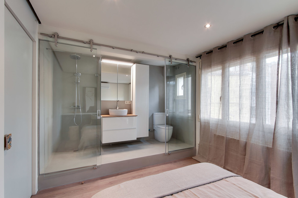 Foto på ett mellanstort funkis badrum med dusch, med släta luckor, vita skåp, en kantlös dusch, en toalettstol med separat cisternkåpa, grå väggar, betonggolv, ett fristående handfat och träbänkskiva