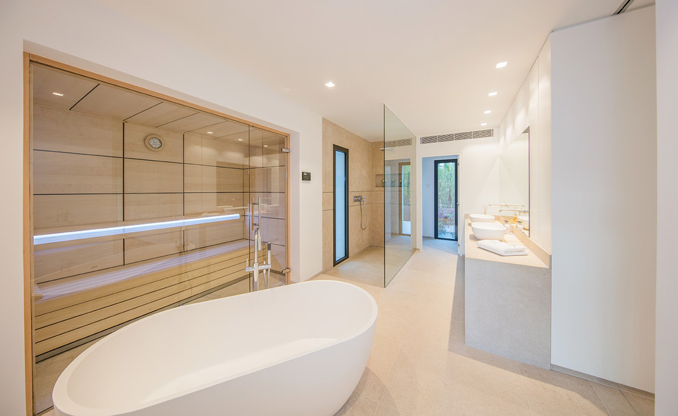 Réalisation d'un très grand sauna minimaliste avec une baignoire indépendante, une douche à l'italienne, un mur blanc, une vasque, un plan de toilette en calcaire et un sol beige.