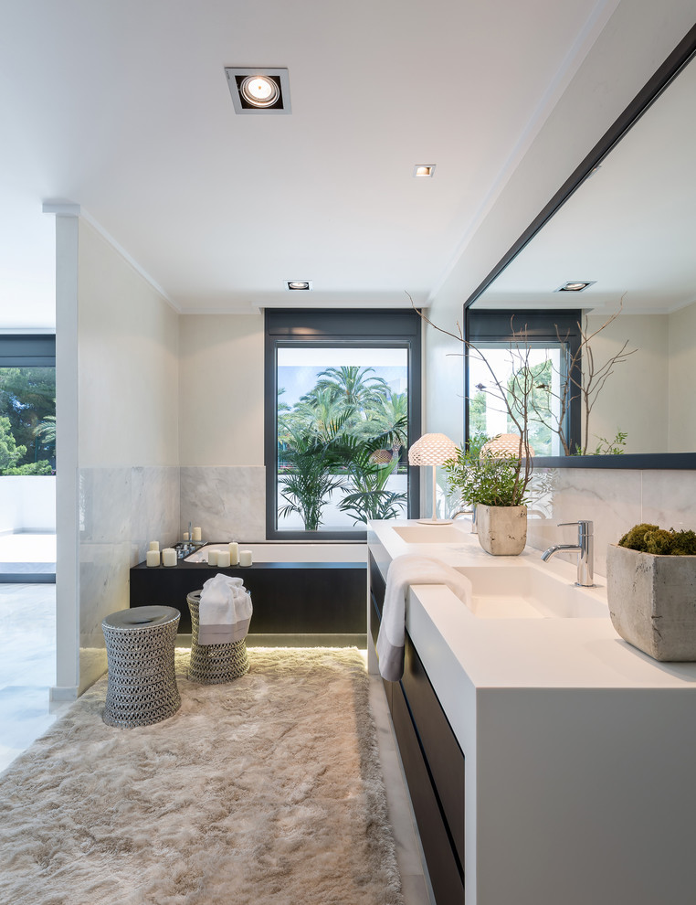 Стильный дизайн: большая главная ванная комната в современном стиле с плоскими фасадами, белой плиткой, белыми стенами, монолитной раковиной, темными деревянными фасадами и полновстраиваемой ванной - последний тренд