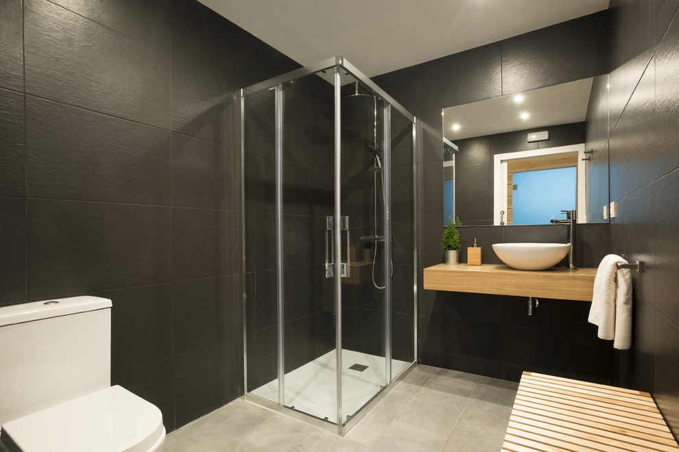 Mid-sized danish 3/4 ceramic tile corner shower photo in Other with a two-piece toilet, black walls, a vessel sink and wood countertops