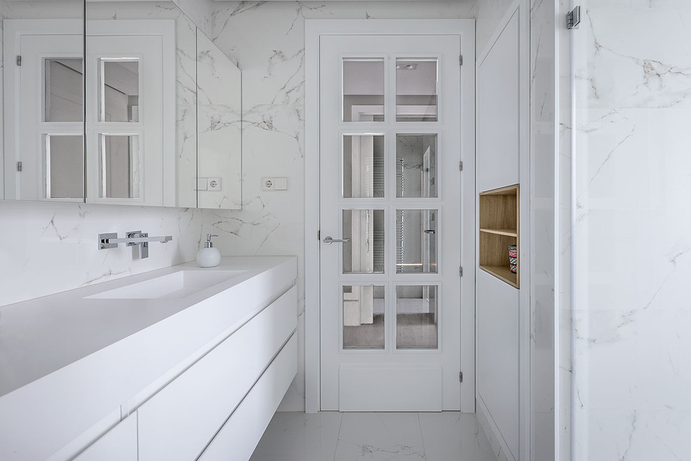 Mid-sized transitional master white tile and ceramic tile marble floor doorless shower photo in Bilbao with recessed-panel cabinets, white cabinets, a wall-mount toilet, white walls, an integrated sink and solid surface countertops