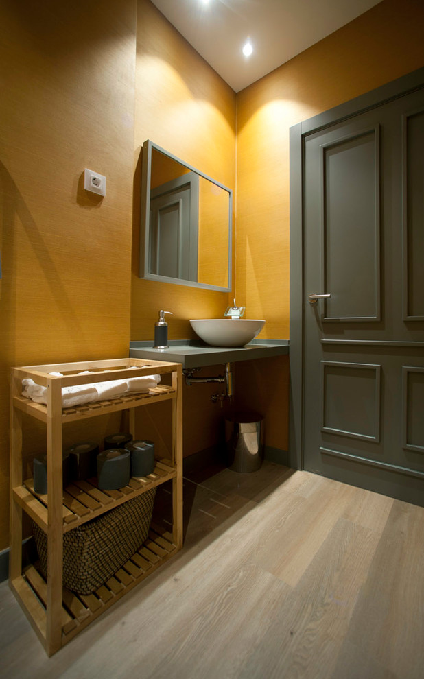 Inspiration for a scandinavian bathroom in Bilbao with open cabinets, light wood cabinets, a wall mounted toilet, yellow tiles, yellow walls, laminate floors, a vessel sink, wooden worktops and grey floors.