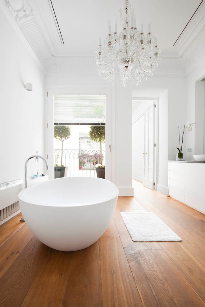 Inredning av ett klassiskt stort en-suite badrum, med släta luckor, vita skåp, ett fristående badkar, en dusch/badkar-kombination, vita väggar, mellanmörkt trägolv och ett fristående handfat