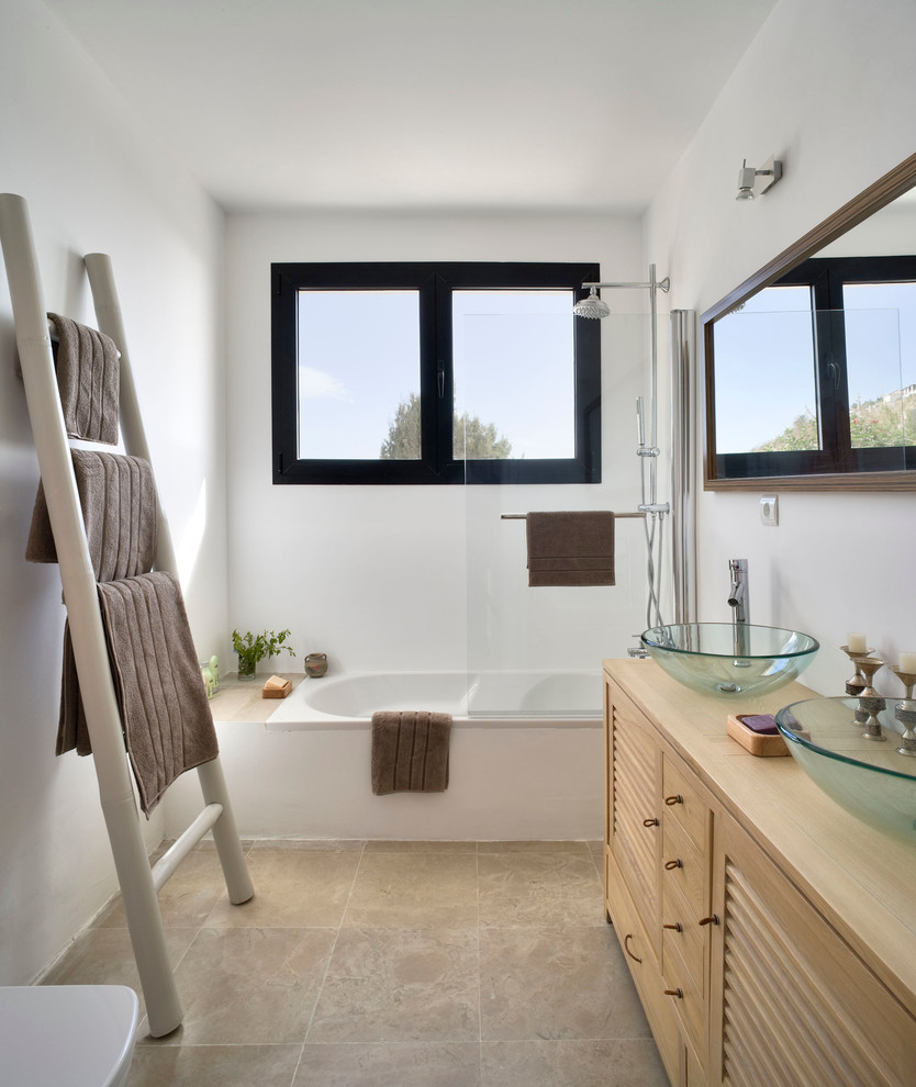 Свежая идея для дизайна: главная ванная комната среднего размера в средиземноморском стиле с настольной раковиной, фасадами с филенкой типа жалюзи, светлыми деревянными фасадами, столешницей из дерева, ванной в нише, душем над ванной, белыми стенами, полом из травертина, бежевой столешницей и зеркалом с подсветкой - отличное фото интерьера