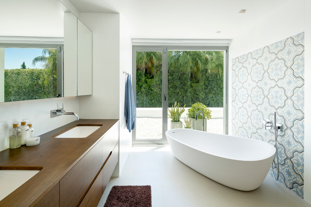 Idéer för att renovera ett funkis en-suite badrum, med släta luckor, ett fristående badkar, vita väggar, ett undermonterad handfat, träbänkskiva, skåp i mellenmörkt trä och flerfärgad kakel