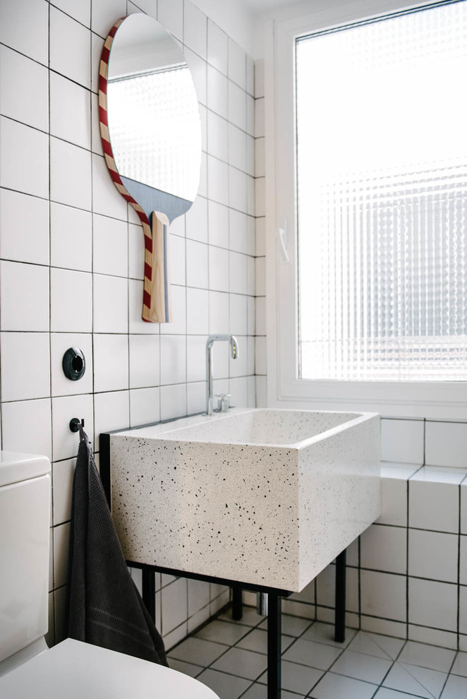 Inredning av ett modernt badrum med dusch, med öppna hyllor, vit kakel, bänkskiva i terrazo, vitt golv, vita väggar och ett konsol handfat