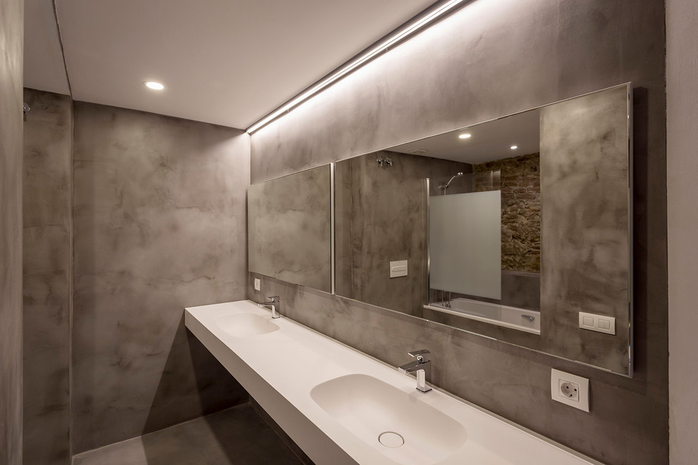 Cette photo montre une salle de bain tendance de taille moyenne avec une baignoire en alcôve, un carrelage beige, un mur gris, sol en béton ciré et un sol gris.