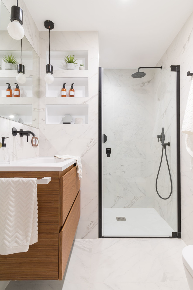 Cette image montre une salle de bain design en bois brun avec un lavabo intégré, un placard à porte plane, un carrelage blanc, du carrelage en marbre, un mur blanc, un sol en marbre, un sol blanc, une cabine de douche à porte battante et un plan de toilette blanc.