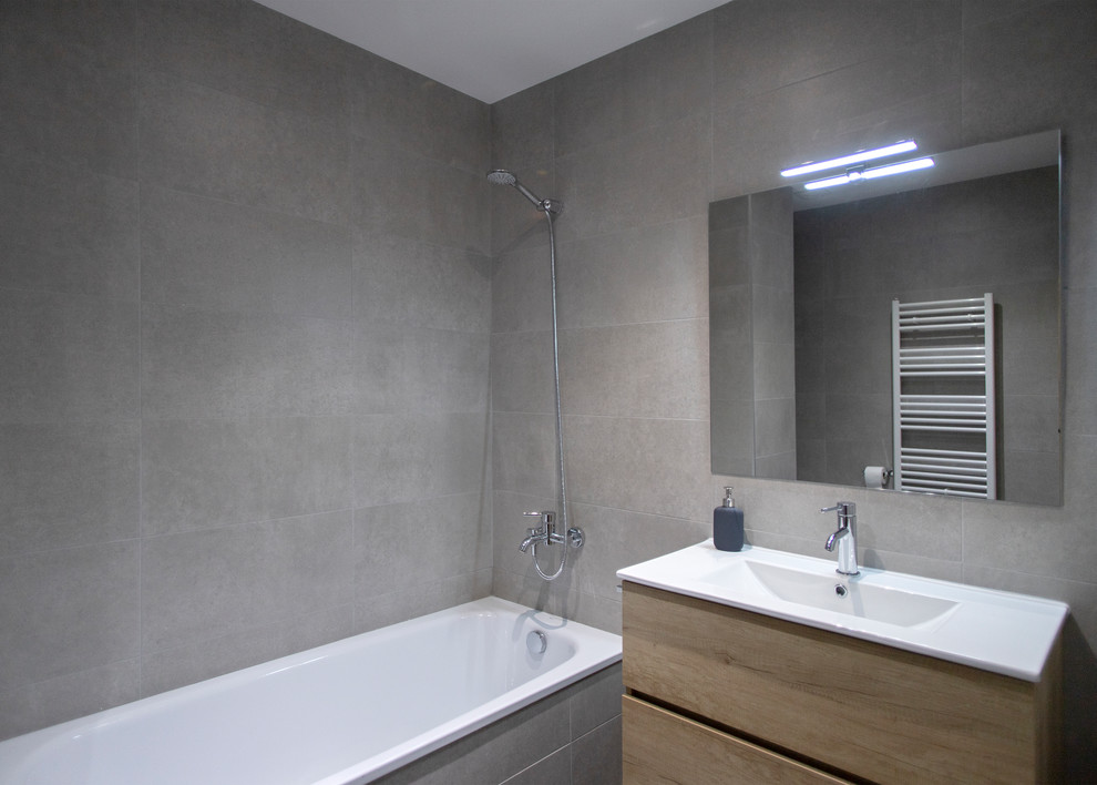 バルセロナにある中くらいなコンテンポラリースタイルのおしゃれなマスターバスルーム (フラットパネル扉のキャビネット、中間色木目調キャビネット、アルコーブ型浴槽、一体型トイレ	、グレーのタイル、グレーの床、オープンシャワー、白い洗面カウンター) の写真