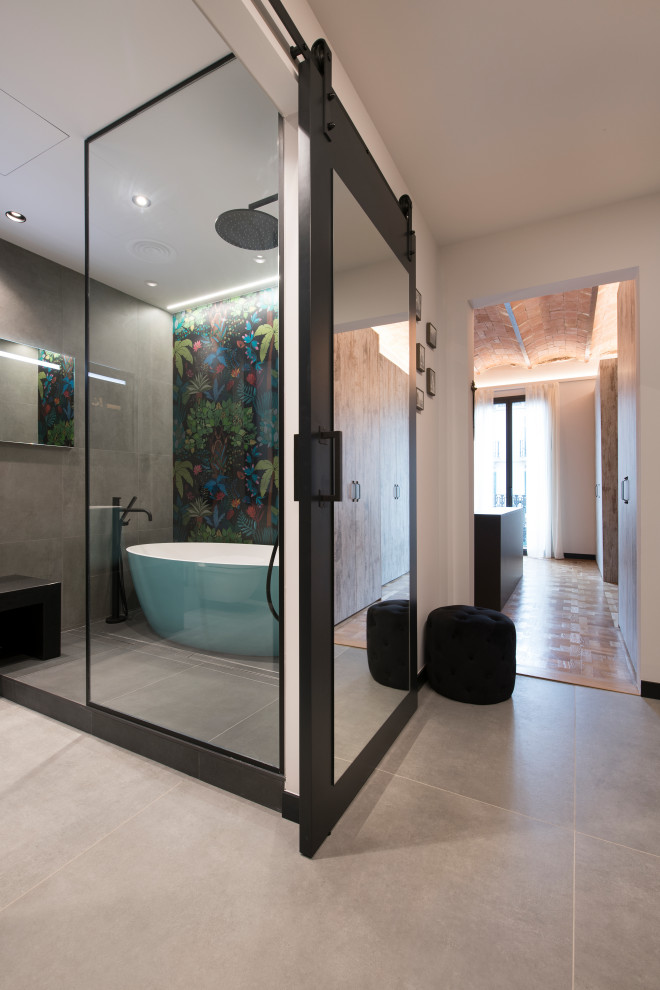 Expansive urban ensuite bathroom in Other with open cabinets, turquoise cabinets, a freestanding bath, a built-in shower, a wall mounted toilet, grey tiles, porcelain tiles, grey walls, porcelain flooring, a vessel sink, grey floors, black worktops, an enclosed toilet, a single sink and a floating vanity unit.
