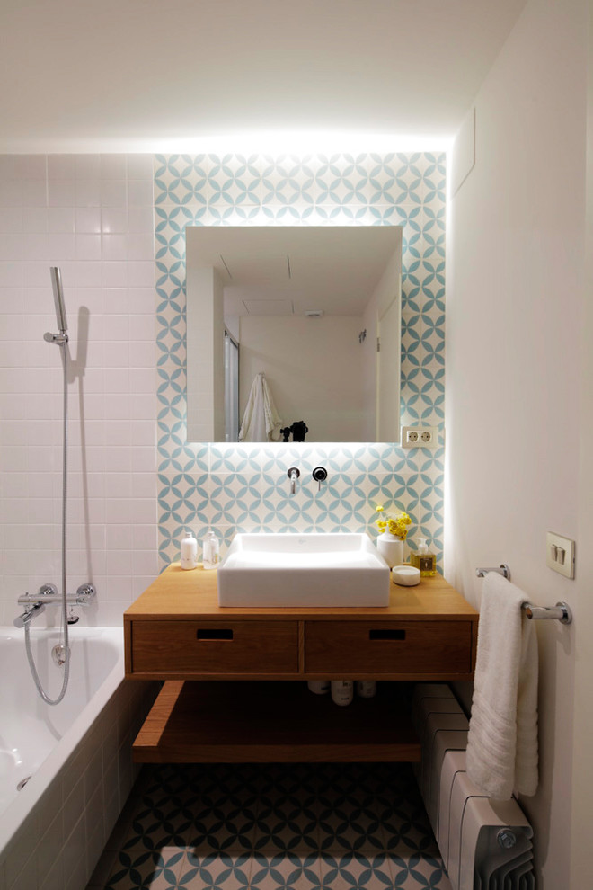 Modelo de cuarto de baño principal actual con baldosas y/o azulejos de cerámica, lavabo sobreencimera, encimera de madera y espejo con luz