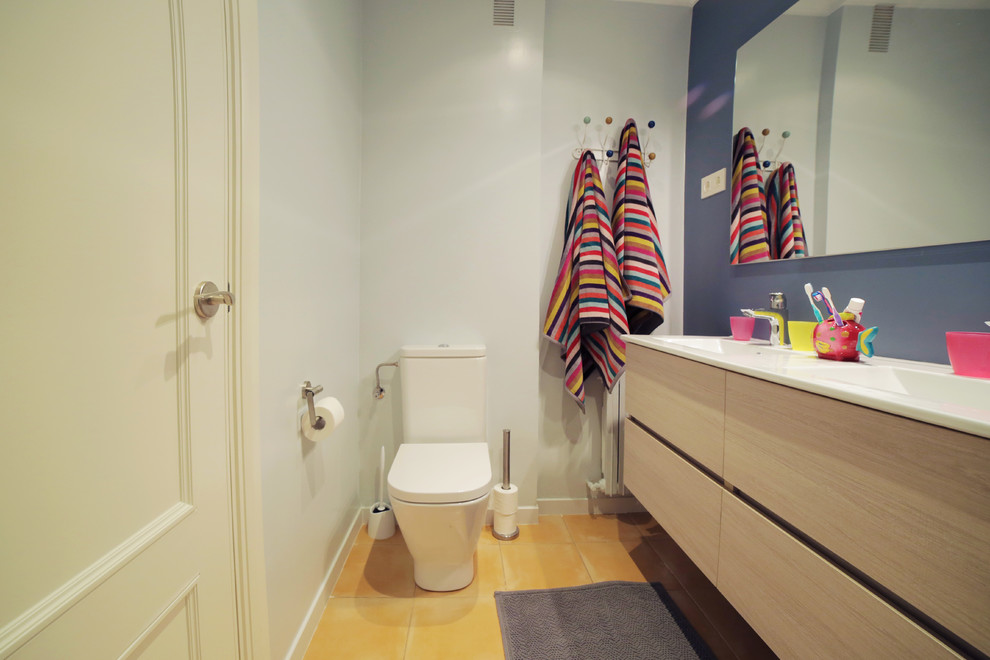 Réalisation d'une salle de bain design en bois clair de taille moyenne pour enfant avec un placard à porte plane, une baignoire posée, un mur bleu, un sol en carrelage de céramique, un lavabo suspendu, un plan de toilette en surface solide et un sol jaune.