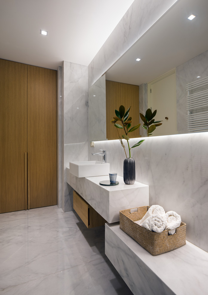 Bild på ett funkis badrum, med skåp i mellenmörkt trä, vit kakel, marmorkakel, vita väggar, marmorgolv, ett fristående handfat, marmorbänkskiva, vitt golv och släta luckor