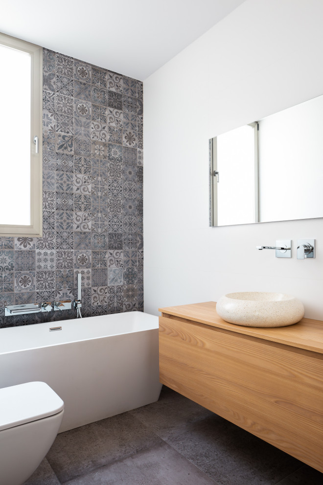 Réalisation d'une salle d'eau design en bois brun de taille moyenne avec un placard à porte plane, une baignoire indépendante, WC suspendus, un carrelage gris, un mur blanc, une vasque, un plan de toilette en bois, un sol gris et un plan de toilette beige.