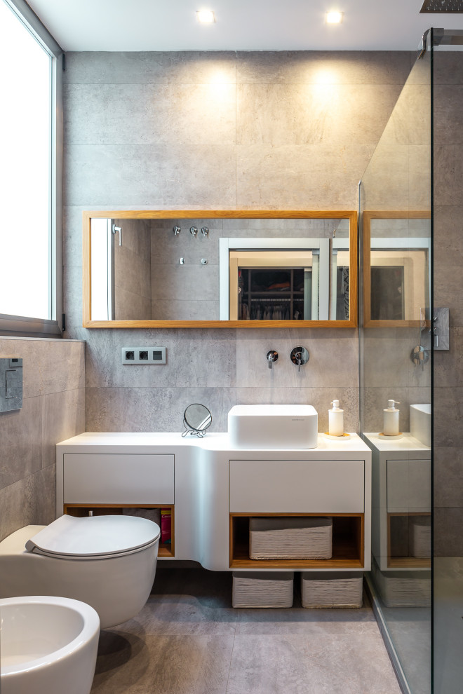 Пример оригинального дизайна: ванная комната среднего размера в современном стиле с плоскими фасадами, белыми фасадами, угловым душем, инсталляцией, серой плиткой, керамогранитной плиткой, полом из керамогранита, душевой кабиной, настольной раковиной, серым полом и белой столешницей