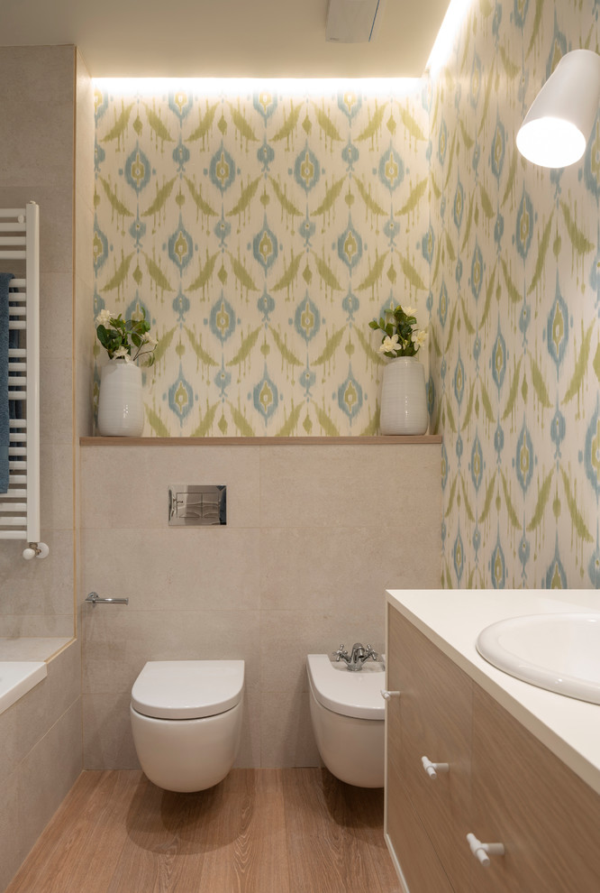 Inspiration pour une grande salle de bain principale design en bois clair avec un placard en trompe-l'oeil, une baignoire en alcôve, un bidet, un carrelage beige, des carreaux de porcelaine, un mur bleu, sol en stratifié, une vasque, un plan de toilette en bois, un sol marron et un plan de toilette blanc.