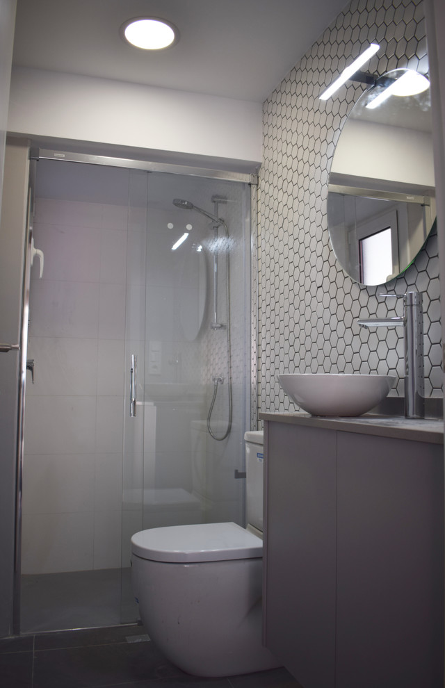 Cette image montre une petite salle de bain avec des portes de placard grises, WC suspendus, un carrelage gris, un mur blanc, un sol en carrelage de céramique, une vasque, un plan de toilette en terrazzo, un sol gris, une cabine de douche à porte coulissante et un plan de toilette gris.