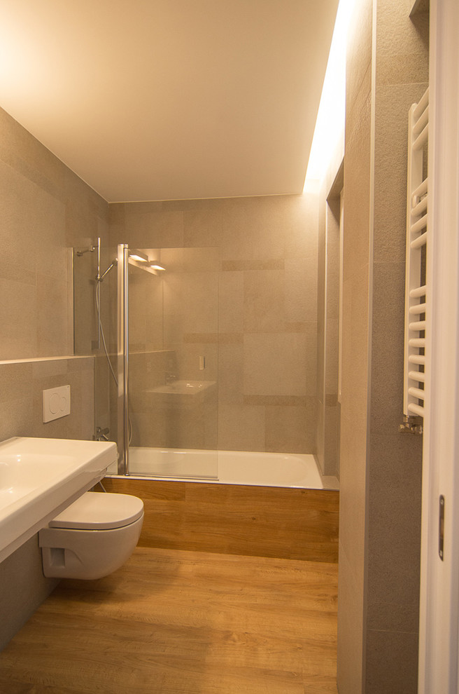 Imagen de cuarto de baño contemporáneo de tamaño medio con bañera empotrada, combinación de ducha y bañera, sanitario de pared, paredes grises, suelo de madera en tonos medios, aseo y ducha y lavabo suspendido