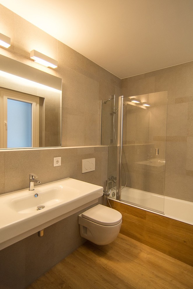 Ejemplo de cuarto de baño principal contemporáneo de tamaño medio con bañera empotrada, combinación de ducha y bañera, sanitario de pared, paredes grises, suelo de madera en tonos medios y lavabo suspendido