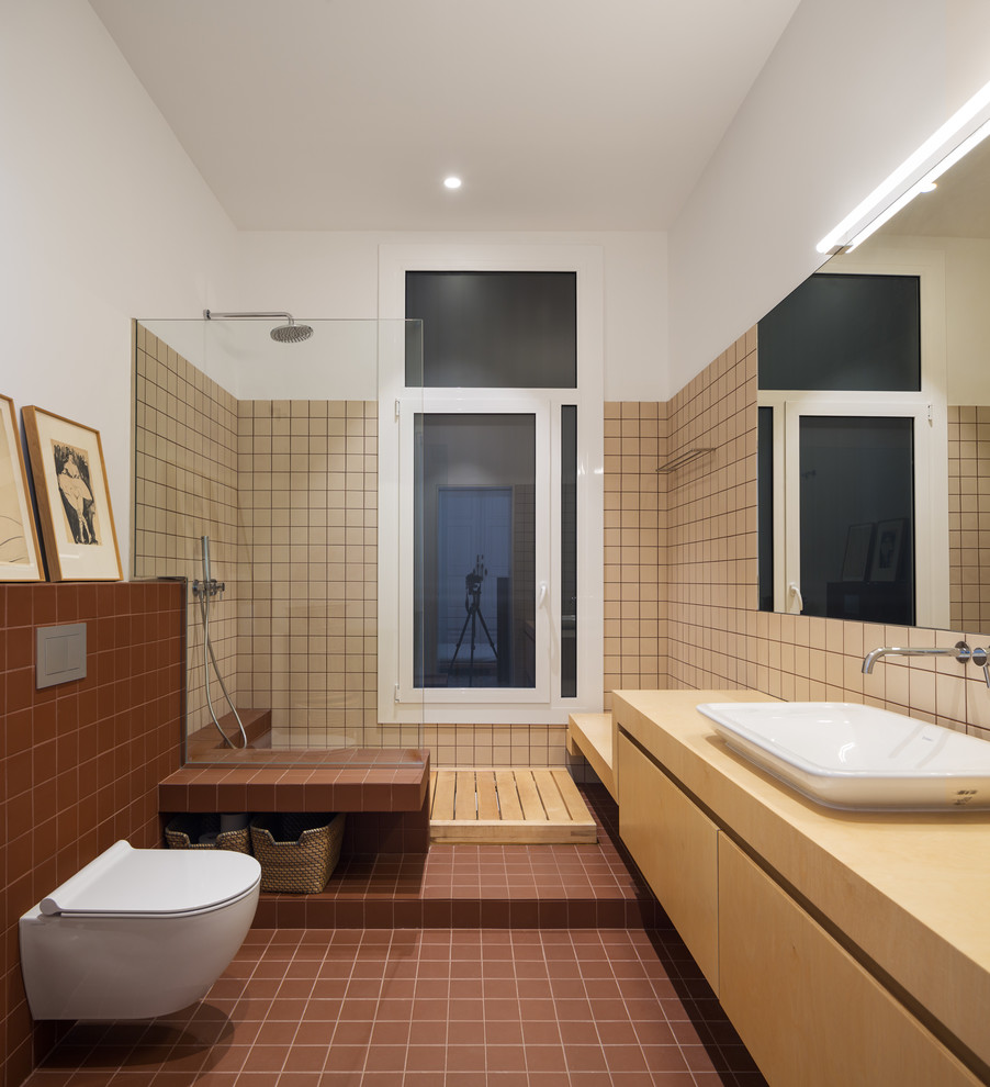 Inspiration for a mediterranean shower room bathroom in Barcelona with flat-panel cabinets, light wood cabinets, a corner shower, a wall mounted toilet, beige tiles, white walls, cement flooring, a built-in sink, wooden worktops, brown floors, an open shower and beige worktops.