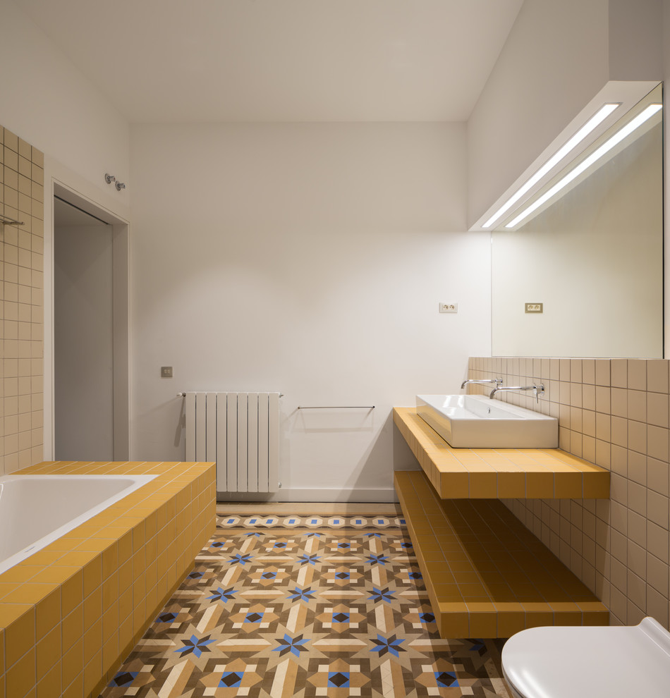 Идея дизайна: ванная комната в средиземноморском стиле с желтыми фасадами, накладной ванной, инсталляцией, бежевой плиткой, цементной плиткой, белыми стенами, душевой кабиной, раковиной с несколькими смесителями, разноцветным полом и желтой столешницей