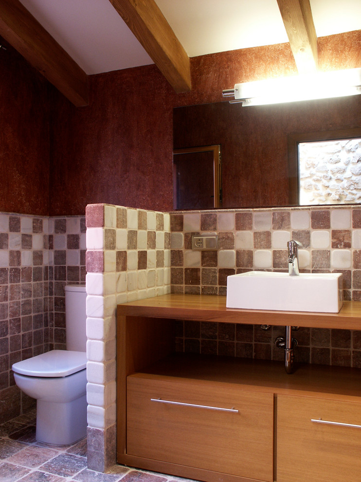 Exemple d'une salle de bain principale méditerranéenne en bois brun avec un placard à porte plane, une baignoire en alcôve, un combiné douche/baignoire, WC séparés, un carrelage multicolore, un carrelage de pierre, un mur violet, un sol en travertin, une vasque et un plan de toilette en bois.