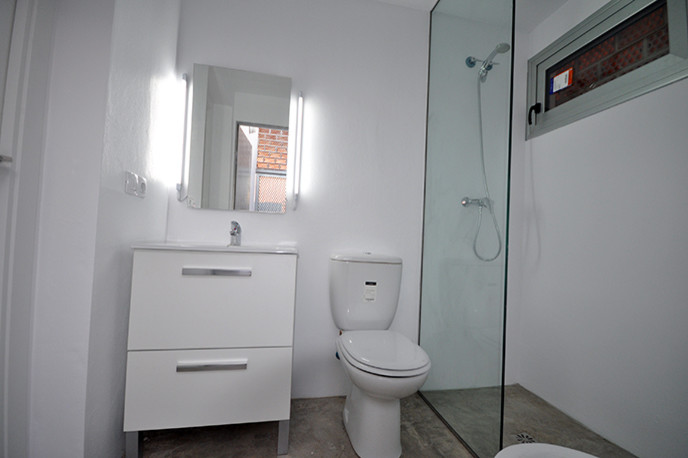Foto på ett litet vintage badrum med dusch, med släta luckor, vita skåp, en kantlös dusch, en toalettstol med separat cisternkåpa, vita väggar och ett integrerad handfat