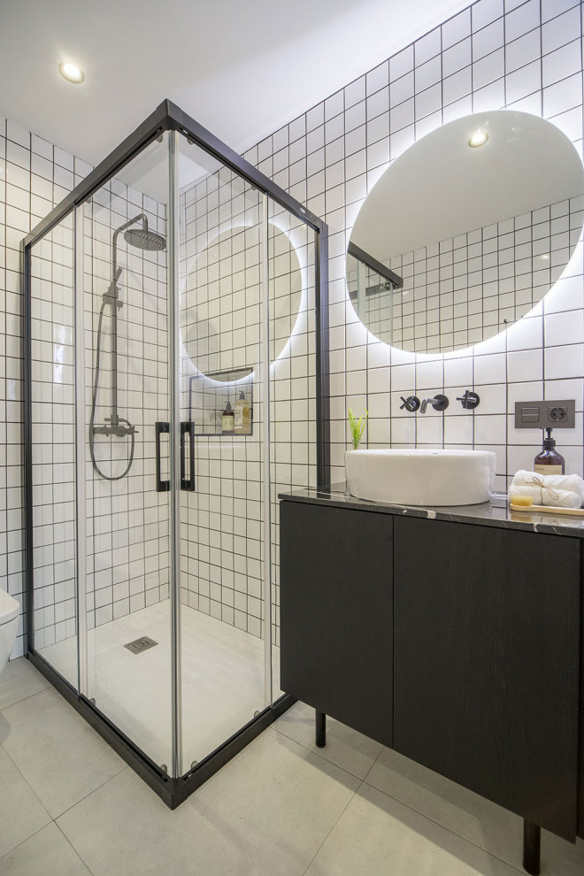 Bild på ett funkis grå grått badrum, med släta luckor, svarta skåp, en hörndusch, vit kakel, ett fristående handfat, grått golv och dusch med skjutdörr