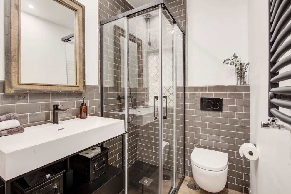 Idéer för att renovera ett litet industriellt vit vitt badrum med dusch, med en hörndusch, en vägghängd toalettstol, grå kakel, laminatgolv, ett avlångt handfat, bänkskiva i akrylsten, brunt golv, dusch med skjutdörr, tunnelbanekakel och vita väggar