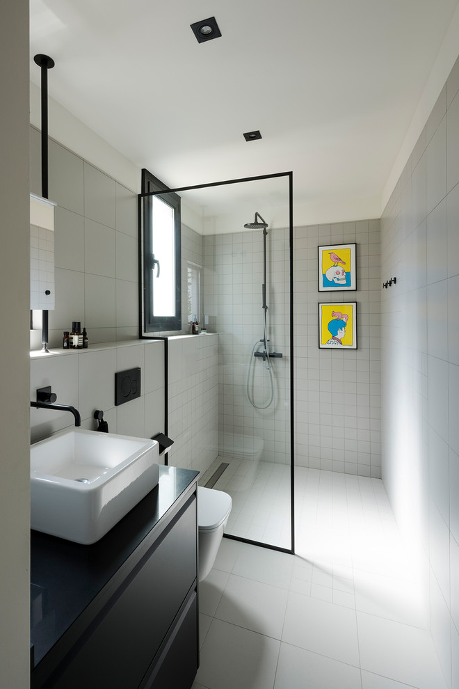 Idéer för att renovera ett mellanstort funkis badrum med dusch, med släta luckor, svarta skåp, en kantlös dusch, en vägghängd toalettstol, grå kakel, keramikplattor, vita väggar, klinkergolv i keramik, ett fristående handfat, grått golv och dusch med gångjärnsdörr