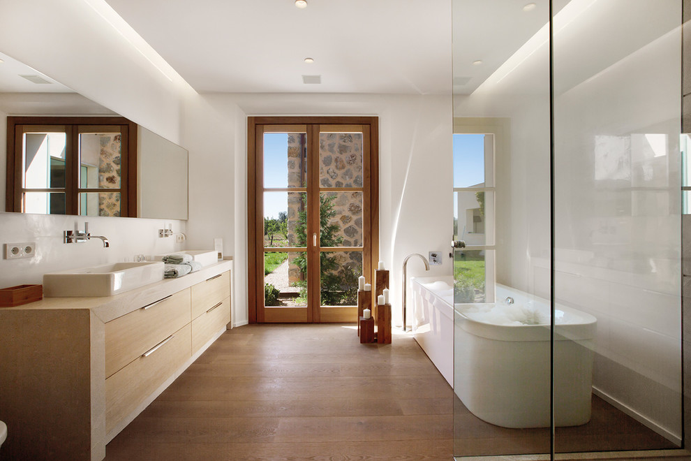 Idéer för mellanstora medelhavsstil en-suite badrum, med ett fristående handfat, släta luckor, beige skåp, ett fristående badkar, vita väggar, mellanmörkt trägolv och brunt golv