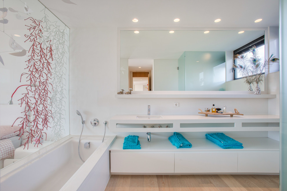 Ejemplo de cuarto de baño principal actual con puertas de armario blancas, bañera encastrada, paredes blancas, lavabo encastrado, encimeras blancas y armarios con paneles lisos