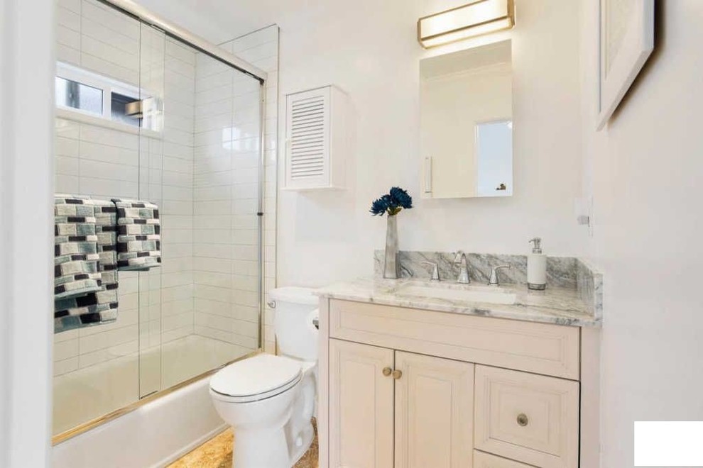 Photo of a small contemporary shower room bathroom in Los Angeles with freestanding cabinets, beige cabinets, a built-in bath, a shower/bath combination, a one-piece toilet, beige tiles, ceramic tiles, white walls, ceramic flooring, a trough sink, granite worktops, beige floors, a sliding door and multi-coloured worktops.