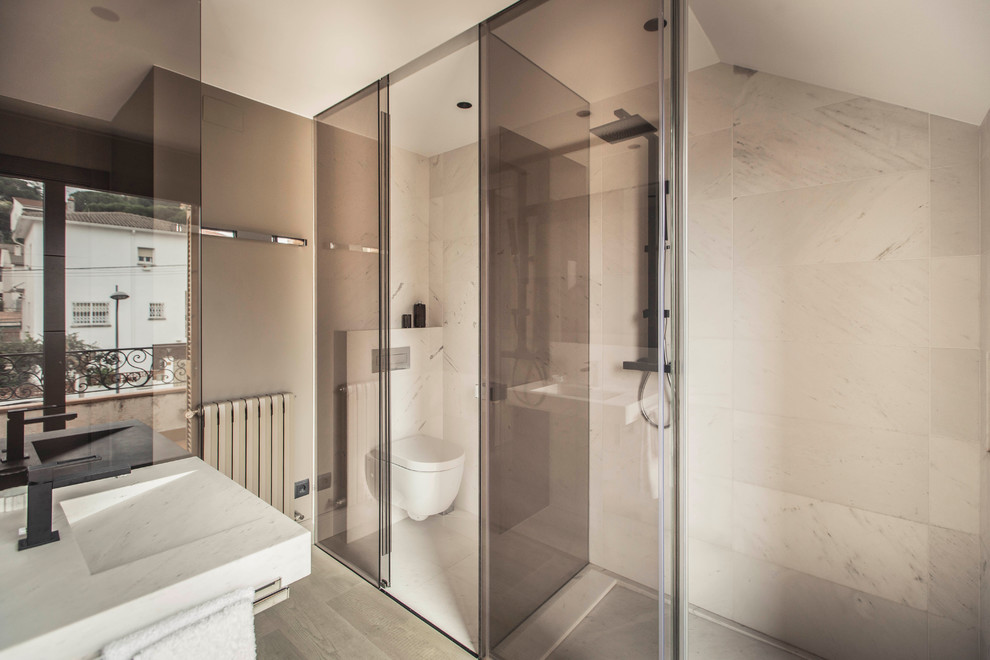 Modern inredning av ett mellanstort en-suite badrum, med möbel-liknande, skåp i mellenmörkt trä, en kantlös dusch, en vägghängd toalettstol, vit kakel, vita väggar, mellanmörkt trägolv, ett väggmonterat handfat och marmorbänkskiva