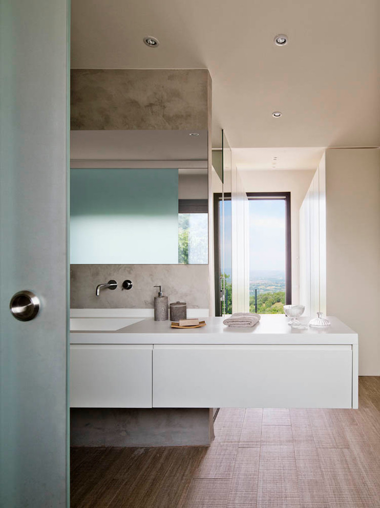 Diseño de cuarto de baño minimalista de tamaño medio con armarios con paneles lisos, puertas de armario blancas, paredes grises, suelo de madera en tonos medios, aseo y ducha, lavabo integrado, encimera de acrílico y microcemento