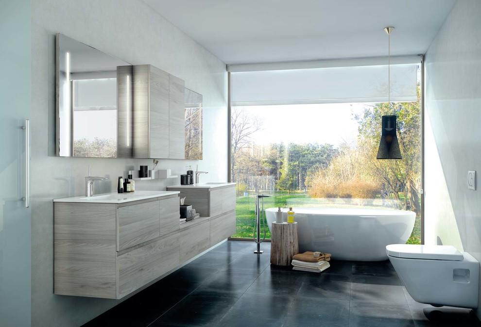 Modelo de cuarto de baño principal contemporáneo de tamaño medio con armarios con paneles lisos, puertas de armario de madera oscura, bañera exenta, sanitario de pared, paredes blancas y lavabo integrado