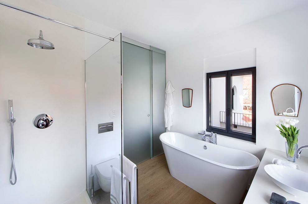 Inredning av ett modernt mellanstort en-suite badrum, med ett fristående badkar, en dusch i en alkov, en vägghängd toalettstol, vit kakel, vita väggar, mellanmörkt trägolv, ett fristående handfat och bänkskiva i betong
