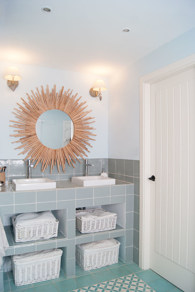 Bild på ett medelhavsstil grå grått badrum, med keramikplattor, öppna hyllor, grå kakel, blå väggar, ett fristående handfat, kaklad bänkskiva och turkost golv