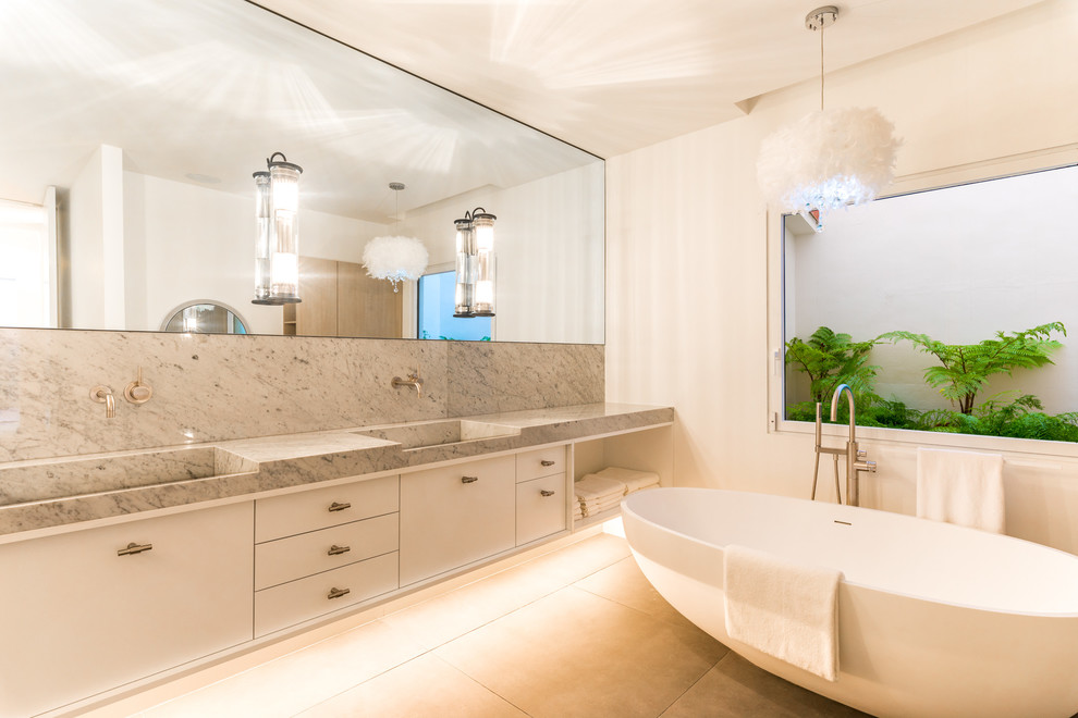 Immagine di una stanza da bagno minimal con ante lisce, ante bianche, vasca freestanding, pareti bianche, pavimento in cemento, lavabo integrato, top in marmo, pavimento grigio e top grigio