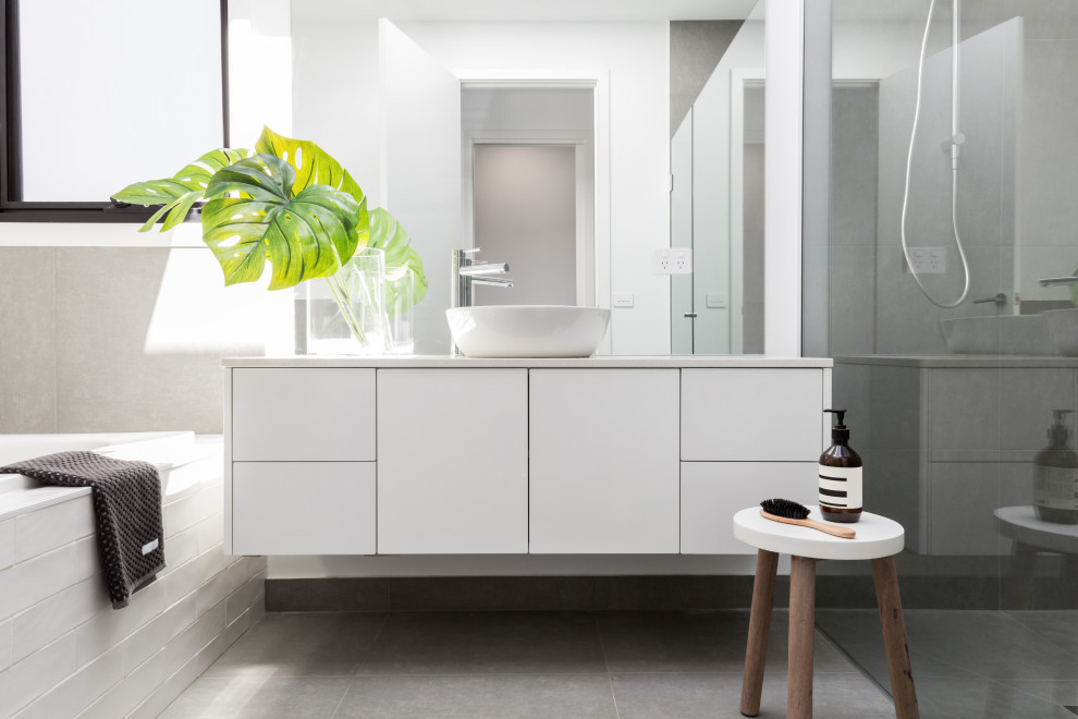 Design ideas for a large modern ensuite bathroom in Malaga with flat-panel cabinets, white cabinets, a built-in bath, a built-in shower, a wall mounted toilet, grey tiles, ceramic tiles, grey walls, porcelain flooring, a vessel sink, engineered stone worktops, grey floors, a hinged door and white worktops.
